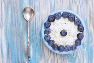 Organic eco healthy meal, dairy product. An overhead photo of fresh natural cottage cheese with silver spoon and blueberries in a blue ceramic bowl on the wooden table. Top view with copyspase.