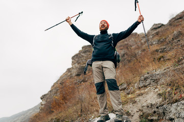 Young tourist male hiking in mountains, finished his track, feels happy. Ttraveler bearded man...