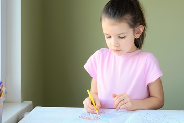 Beautiful caucasian white girl with pony tail paints a picture with colorful wooden pencils. Smiling cute girl in pink T-shirt drawing a picture with pencils on blurred background. Child learning art 