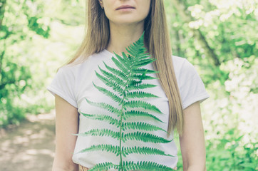 Young woman holds in her hand a leaf of green fern