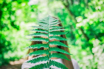 Young woman hides her face behind a large sheet of fern