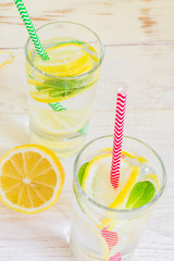glass of homemade lemonade with lemons, mint and paper straws on wooden rustic background. Summer refreshing beverage.