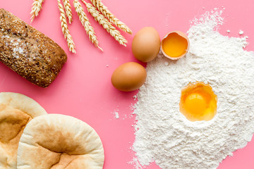 Ingredients for homemade bread. Bread near wheat ears, flour and eggs on pink background top view