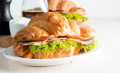 Fresh croissant or sandwich with salad, ham, jamon, prosciutto, salami, cheese, chicken, tomatoes on wooden background. Morning breakfast concept. Healthy and fast food.