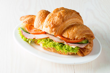 Fresh croissant or sandwich with salad, ham, jamon, prosciutto, salami, cheese, chicken, tomatoes on wooden background. Morning breakfast concept. Healthy and fast food.