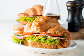 Fresh croissant or sandwich with salad, ham, jamon, prosciutto, salami, cheese, chicken, tomatoes on wooden background. Morning breakfast concept. Healthy and fast food.
