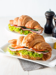 Fresh croissant or sandwich with salad, ham, jamon, prosciutto, salami, cheese, chicken, tomatoes on wooden background. Morning breakfast concept. Healthy and fast food.