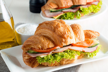Fresh croissant or sandwich with salad, ham, jamon, prosciutto, salami, cheese, chicken, tomatoes on wooden background. Morning breakfast concept. Healthy and fast food.