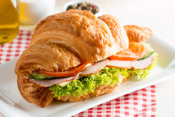 Fresh croissant or sandwich with salad, ham, jamon, prosciutto, salami, cheese, chicken, tomatoes on wooden background. Morning breakfast concept. Healthy and fast food.