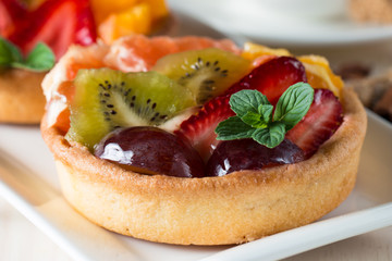 Fresh fruit and berry tart dessert with toss sugar on wooden background. Delicious sweet cake with raspberries, grapes, strawberries, cherry, kiwi, grapefruit and cream.