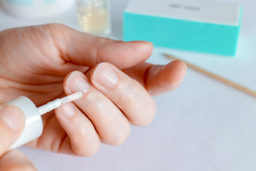 Woman doing at-home manicure, applying oil on cuticles.