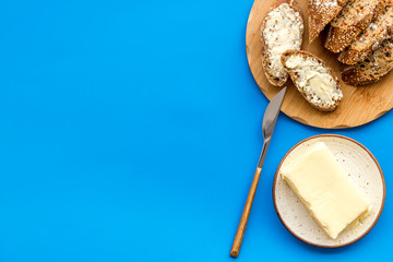 Traditional breakfast. Wholegrain bread on cutting board with butter on plate on blue background top view space for text