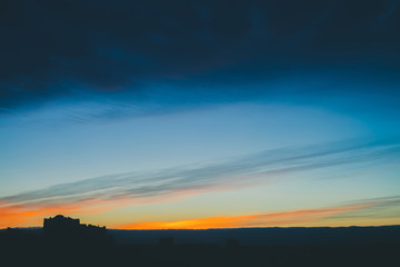 Cityscape with wonderful varicolored vivid dawn. Amazing dramatic blue cloud sky above dark silhouettes of city building roofs. Atmospheric background of orange sunrise in overcast weather. Copy space