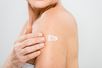 selective focus of mature woman applying cosmetic cream isolated on grey