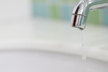 Save the water concept.Hand closing valve on sink in bathroom. Water dripping to stop running as hand turn off the faucet.Detect-a-Leak week.