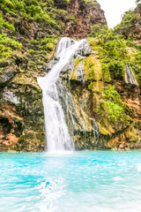Fototapeta na wymiar Waterfall in Ayn Khor and Lush green landscape, trees and foggy mountains at tourist resort, Salalah, Oman