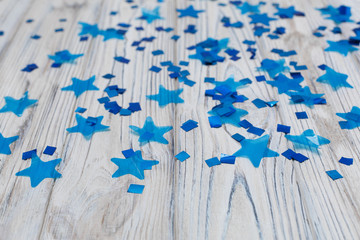 blue shiny stars on a wooden background abstraction. Abstract colorful background with blue elements on a light background. Top view of a train of confetti blue stars on a wooden  background
