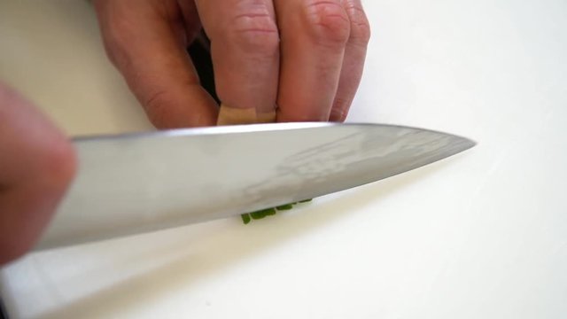Cocinero corta cebollino con un cuchillo en camara lenta y en plano de detalle