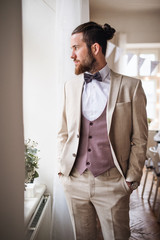 A handsome hipster young man with formal suit standing on an indoor party.