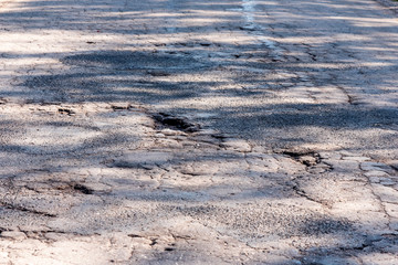 Broken empty asphalt country road surrounded by trees in sunny summer day. Road with holes in the green wood. A hole in the road.