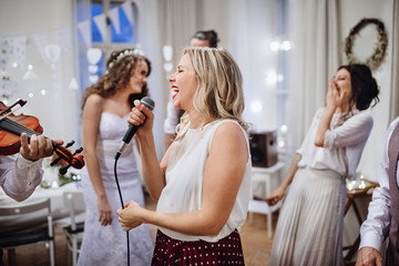 A young woman singing on a wedding reception, bride and guests dancing.
