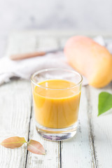 Tropical Mango smoothie in a glass and fresh mango on a light background. Mango shake. Tropical fruit concept.