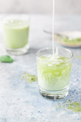 Iced Matcha green latte in glasses with matcha powder on light background.