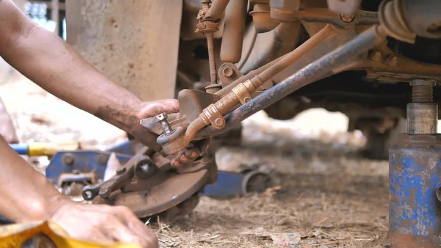 Hands of mechanical spinning bolt of the truck to repair wishbone control arm and replace the front wheel of the car