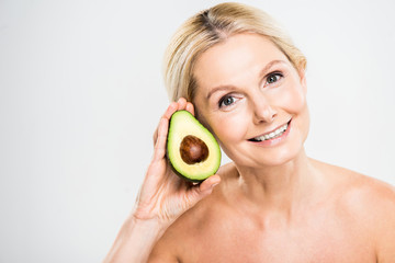 beautiful and smiling woman holding avocado and looking at camera on grey background