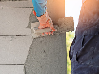 Hand of a man holds a trowel for plastering a cement wall in construction site