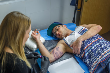Obraz premium A boy with glasses and blue cap is tattooed by a young woman in her tattoo studio