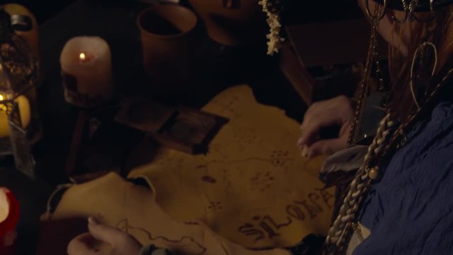 Female Pirate reading a map on a table with candles