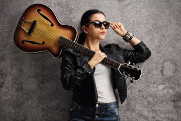 Female guitar player leaning on a rusty gray wall