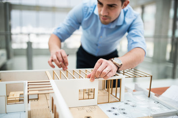 Young businessman or architect with model of a house standing in office, working. - obrazy, fototapety, plakaty
