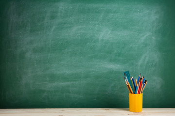 Education concept - school supplies on the desk in the auditorium, blackboard background
