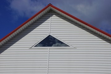 part of the house with a white attic and a small window against the sky and clouds