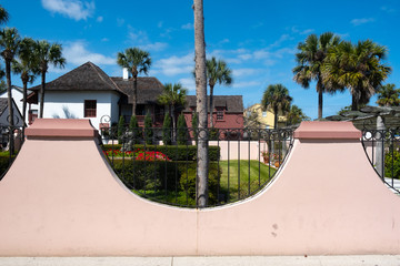 Obraz premium Half oval pink wall with wrought iron fence against a deep blue sky, palm trees and a home