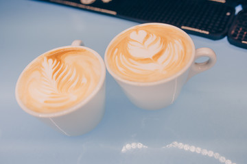 Two white cups of tasty cappucino with art latte heart style for romantic on wooden table in dining restaurant