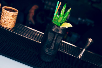 Sweet Famous juicy Pina Colada with ananas Pineapple slice Author inspired Cocktail Drink -on bar counter . Close-up Top view in Statue Humanoid Rocks Vase and luxury service barman in nightclub