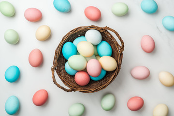 Fototapeta na wymiar top view of scattered pastel easter eggs and wicker basket on white