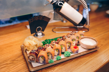 Sushi Smoked Philly plateau buffet in night dining  with bottle of champagne flat lay. Delicious Philadelphia salmon flesh seaweed and ginger. Rolls served on  plate in a restaurant. The norwegian sa