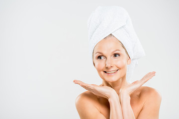 attractive and smiling mature woman in towel looking away isolated on grey