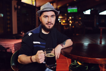 a man in a Bavarian hat drinking beer in a pub and watching football on a monitor during Oktoberfest