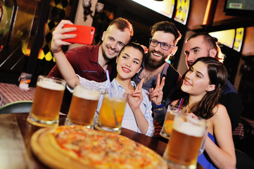 group or company of friends - young guys and girls eat pizza and drink beer in a bar, communicate and laugh.
