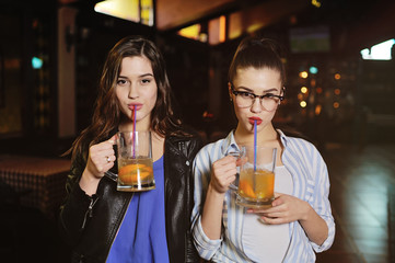 two young cute seductive girls with a glass of beer or a beer cocktail on the background of the bar