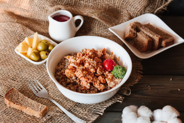 Russian traditional dish, healthy food, proper nutrition. Boiled Buckwheat with minced pork, tomato, broccoli in a white plate and sliced ​​bread next to a wooden background.