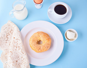 Fresh healthy bagel on a white plate with cup of coffee, cream cheese and eggs for breakfast. Top view.