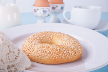 Fresh healthy bagel on a white plate with cup of coffee, cream cheese and eggs for breakfast