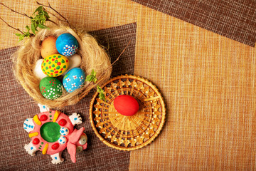 Easter still life. A nest of straw and flax with painted eggs and a rabbit. Wicker basket stands on decorative napkins. Religious Christian holiday..