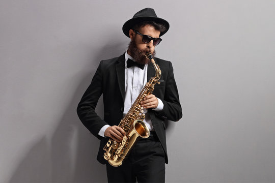 Man Playing A Sax And Leaning Against Gray Wall